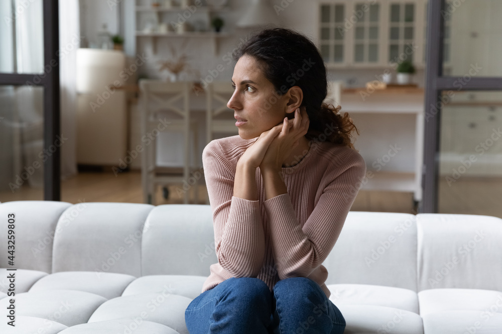 Thoughtful young hispanic woman sitting on sofa in living room, looking in distance, considering problem solution alone indoors. Nervous millennial lady thinking on personal psychological troubles. Thoughtful young hispanic woman sitting on sofa in living room, looking in distance, considering problem solution alone indoors. Nervous millennial lady thinking on personal psychological troubles.