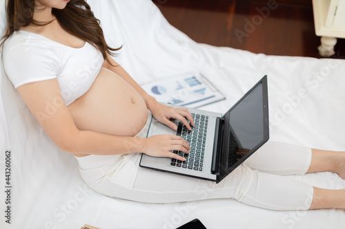 Pregnant business woman sitting and working on the laptop with sale report tablet books and sticky note at home Pregnant of businesswoman typing on laptop Business and Pregnancy Concept