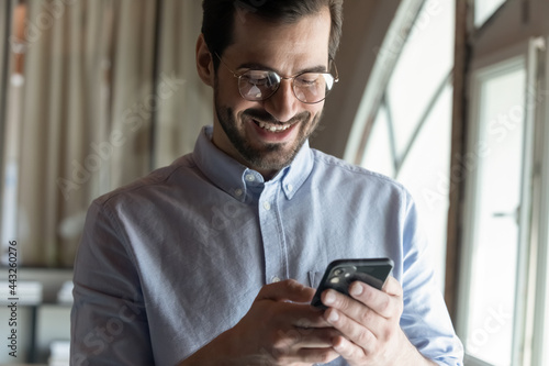 Close up happy businessman in glasses typing and looking at smartphone screen, reading good pleasant news in message, surfing internet, smiling employee entrepreneur chatting online in office