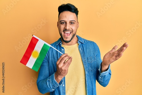 Foto Young arab man holding kurdistan flag celebrating achievement with happy smile a