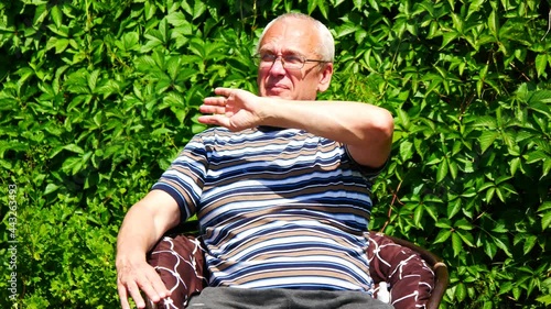 One elderly man with glasses brushes off midges and mosquitoes and then sprays himself with anti insects spray photo
