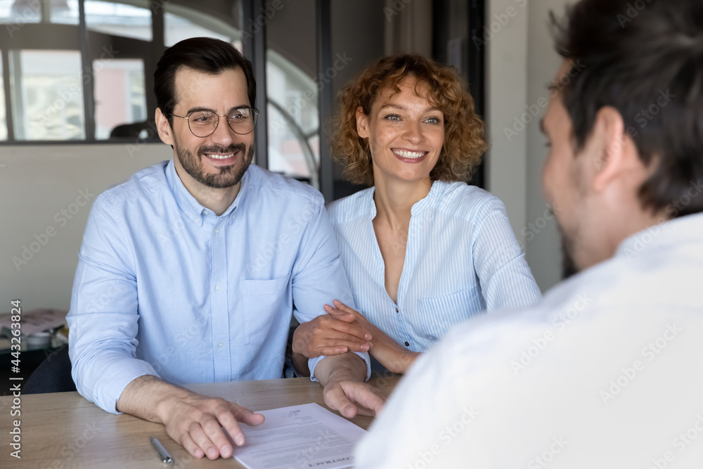 Fototapeta premium Happy young married couple listening to manager at meeting in office, advisor realtor or broker consulting satisfied customers smiling woman and man about contract terms, negotiations concept