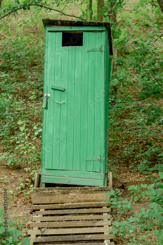 Old green wooden toilet in a rustic style with stairs and solid foundation in the forest. wooden toilet locked in the park. single vertical structure in nature
