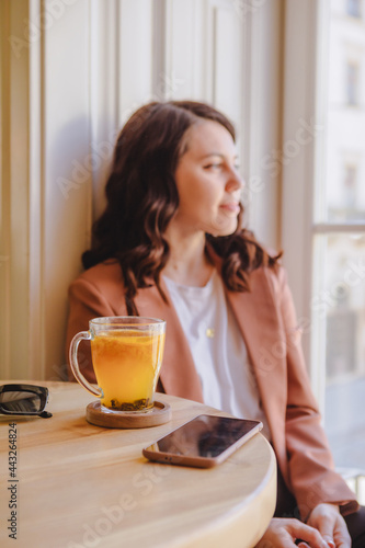 mug with orange tea on the cafe table woman on background