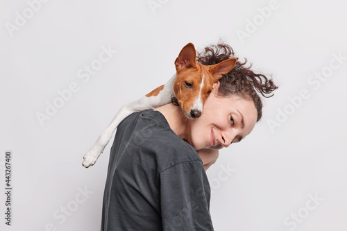 Female pet owner plays with favorite dog which leans on her head being best friends spend time together dressed in casual t shirt isolated over white background. Animals people friendship concept