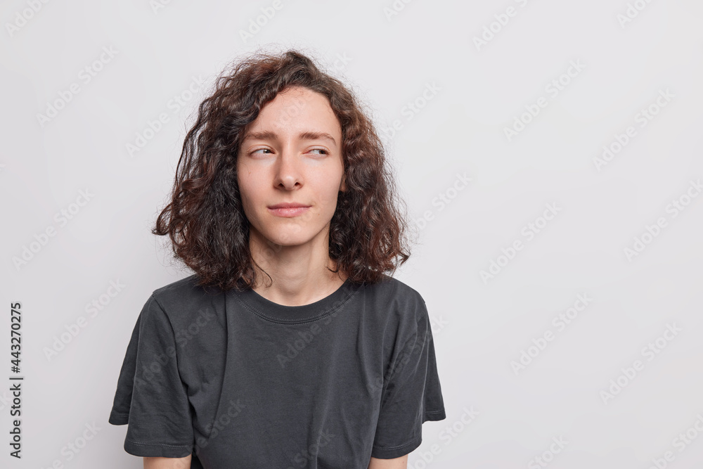 Portrait of mysterious thoughtful young woman with dark hair looks away has doubtful expression wears black t shirt isolated over white background blank copy space on right for your promotion Portrait of mysterious thoughtful young woman with dark hair looks away has doubtful expression wears black t shirt isolated over white background blank copy space on right for your promotion