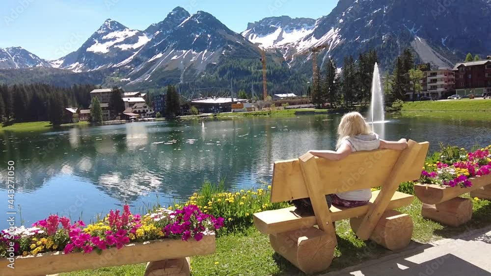 Woman tourist relaxing on a park bench of Arosa town and tourist resort by Obersee Lake in Switzerland. Arosa lakefront by cable car station to Aroser Weisshorn peak. Plessur Region in Grisons Canton.