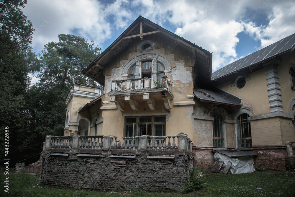 An old beautiful abandoned manor house in the forest. Blue sky with clouds. Green trees and grass. Ancient architecture of an abandoned building. An old beautiful abandoned manor house in the forest. Blue sky with clouds. Green trees and grass. Ancient architecture of an abandoned building.