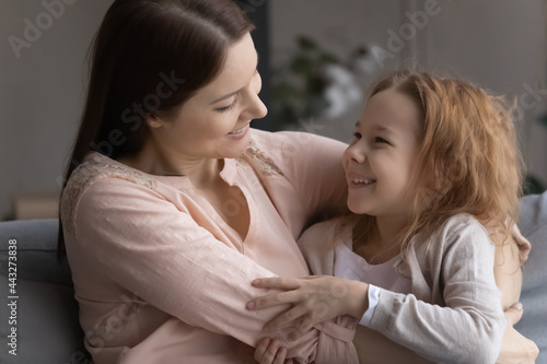 Mommy and me. Caring parent foster mother embrace small adopted child girl on sofa at living room. Bonding family of millennial single mom and preteen daughter good friends hug talk having fun at home