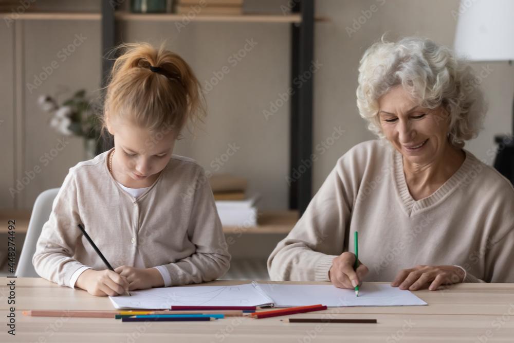 Pleasant old age woman child psychologist doing art therapy session involve little girl patient in drawing picture together. Caring senior grandmother assist preteen grandchild to paint coloring book Pleasant old age woman child psychologist doing art therapy session involve little girl patient in drawing picture together. Caring senior grandmother assist preteen grandchild to paint coloring book