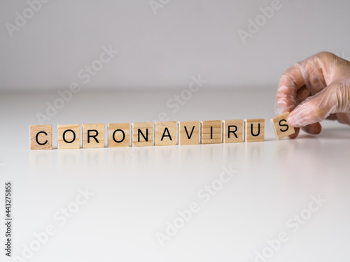coronavirus - napis z drewnianych kostek, ręka w rękawiczce 