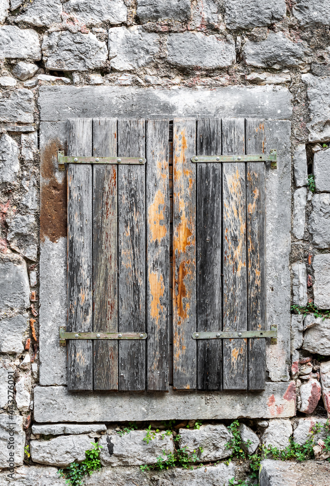 Naklejka premium Window of old stone house is closed by wooden shutters. Close up.
