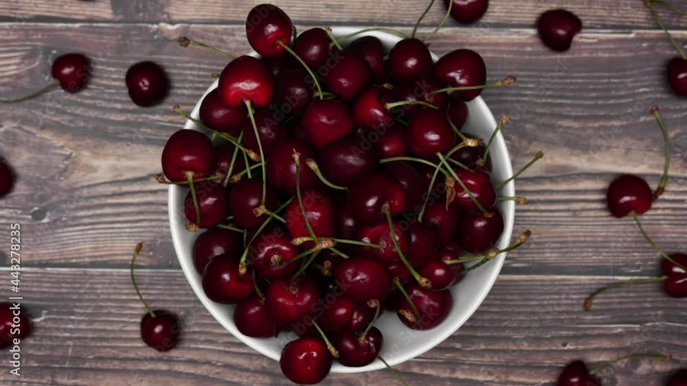 Black Cherry In A White Bowl. Fresh Ripe Berries Fruits Are Scattered On A Wooden Table Background. Rotation Shot. Close Up. Black Cherry In A White Bowl. Fresh Ripe Berries Fruits Are Scattered On A Wooden Table Background. Rotation Shot. Close Up.