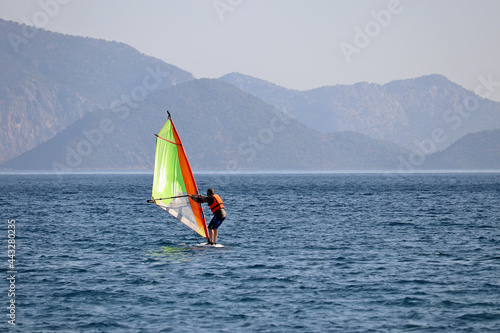 Windsurfing in the sea, water sports. View to windsurfer and green mountains in mist © Oleg