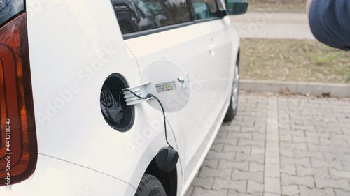 Mans hand unblocking an electric car with a key and diconnect a power cable supply plugged in the elctric vehicle.  photo