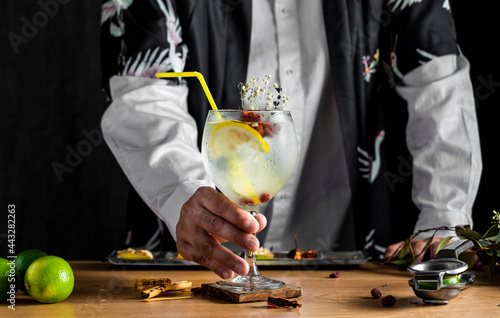  Barman standing behind and holding freshly prepared gin and tonic on a wooden table