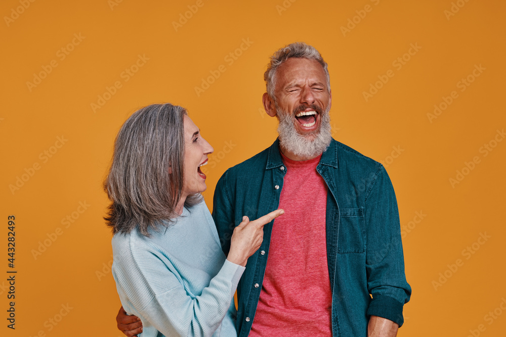 Obraz premium Beautiful senior couple laughing while standing together against orange background