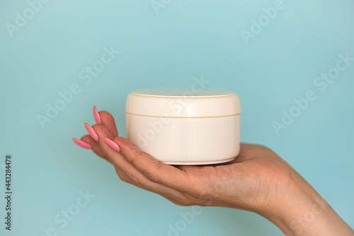 A woman's hand holds a white jar of cosmetic cream.