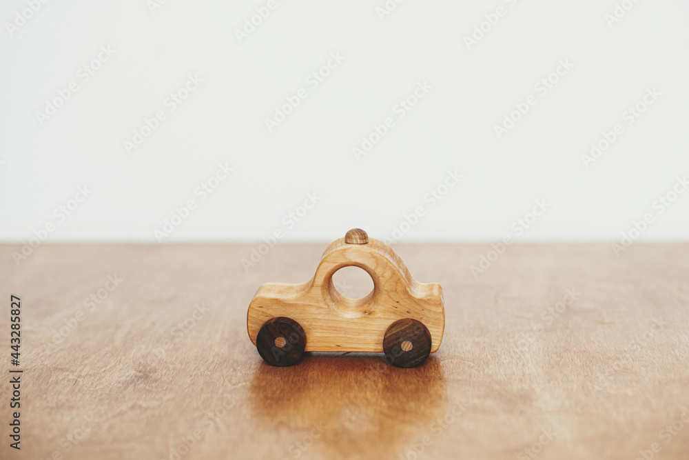 Road trip and travel concept. Stylish natural wooden car toy on table on white wall background. Space for text. Eco friendly plastic free toy for toddler. Stylish simple toy for child