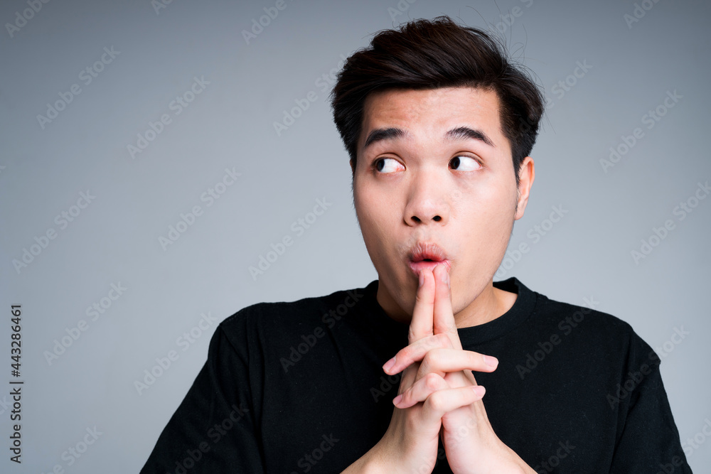 Scared and surprised asian guy puts his fingers to his mouth and looks ...