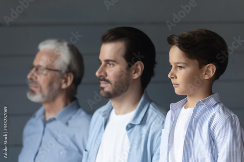 Serious boy, his father and grandpa standing together in row, looking forward. Portrait of three male generations, preschool child, young man, older pensioner. Family relations, heredity concept