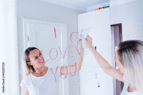 A blonde woman wipes the inscription of red lipstick from the mirror.