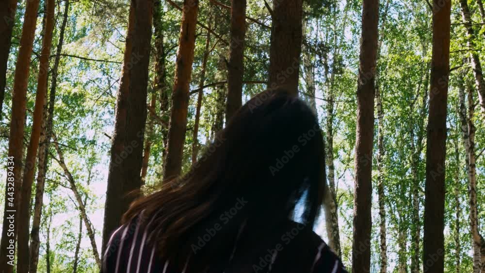 A young woman in a loose summer dress with loose dark hair relaxes in a dance movement in a summer forest. Coniferous forest mixed with birches in the park. A young woman in a loose summer dress with loose dark hair relaxes in a dance movement in a summer forest. Coniferous forest mixed with birches in the park.