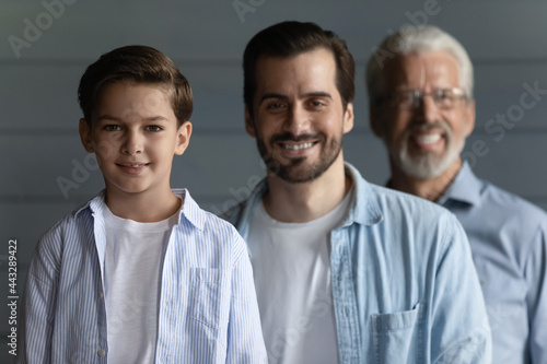 Happy family portrait on three male generations, kid, father and grandfather. Cute preschooler boy, young man, mature pensioner standing in row, looking at camera, smiling. Dynasty concept, Head shot