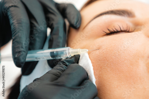 Plastic syrgery. Close-up of female face getting injection in the cosmetology salon. Doctor in medical gloves with syringe injects cheek a botulinum toxin