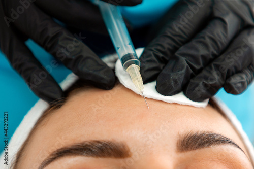 Concept of plastic surgery. Close-up of female s head getting injection in the cosmetology salon. Cosmetologist in latex gloves with syringe injects a botulinum toxin in forehead