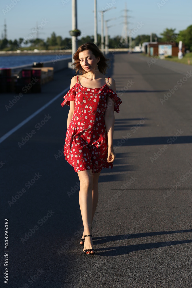 Slender woman in red dress walking by embankment