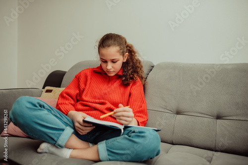 The girl sits in the house and writes homework in a notebook