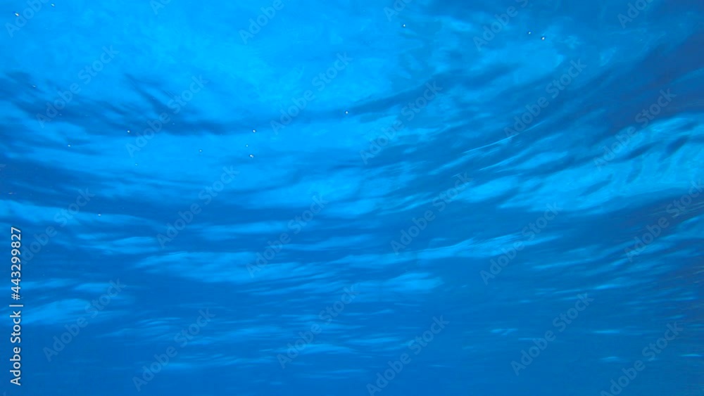 Slow motion, surface of blue water. Natural background with sun glints on surface of blue water. Texture of blue water surface of sea reflection of sun's rays. Underwater shot Slow motion, surface of blue water. Natural background with sun glints on surface of blue water. Texture of blue water surface of sea reflection of sun's rays. Underwater shot