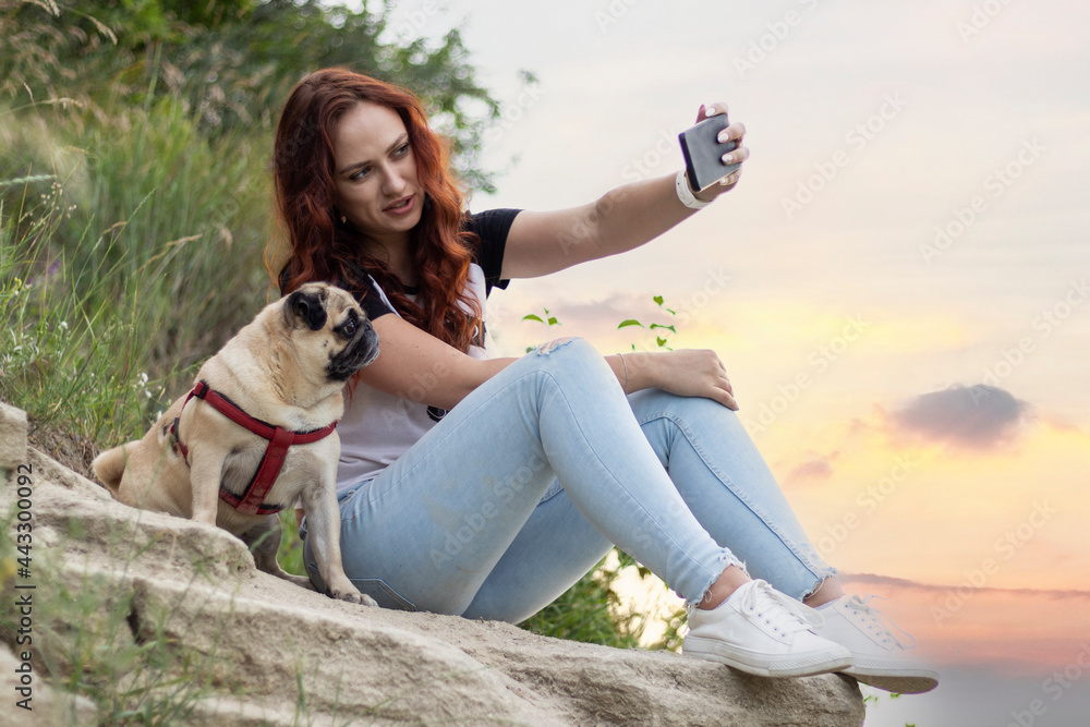 Young red-haired woman taking a selfie photo with her pug dog.