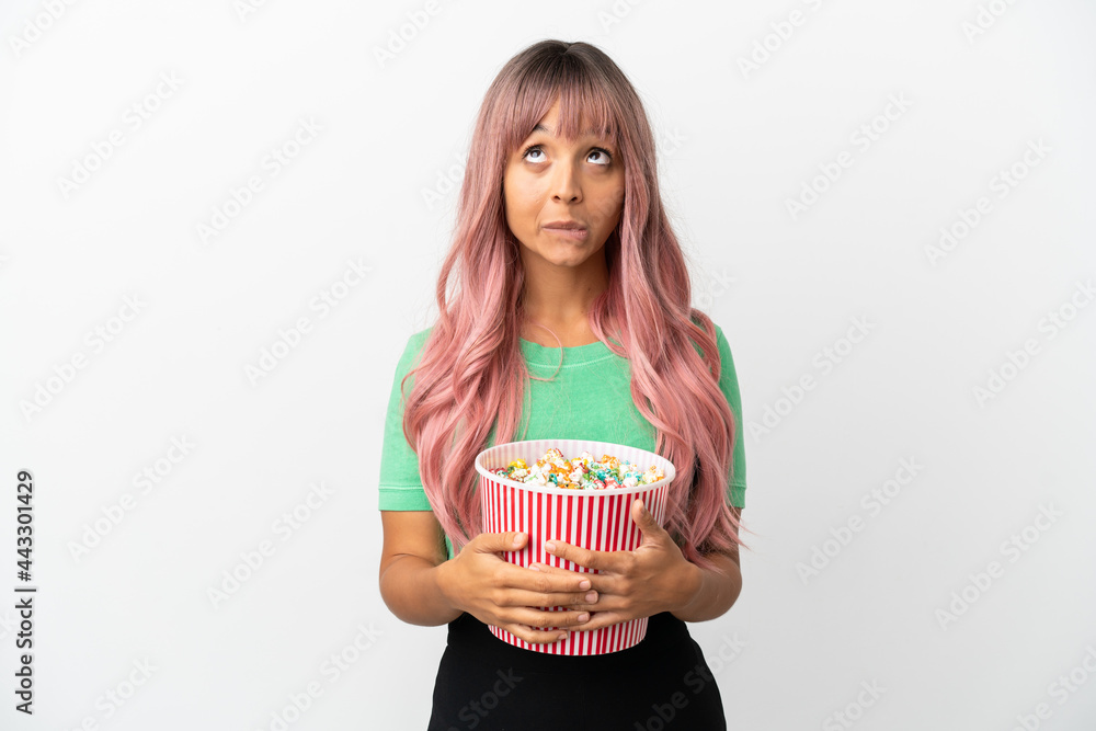Young mixed race woman with pink hair eating popcorn isolated on white background and looking up Young mixed race woman with pink hair eating popcorn isolated on white background and looking up