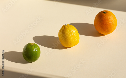 art creative composition of orange, lemon and lime under hard light on beige background, oval harsh shadows of citrus, high angle, diagonal
