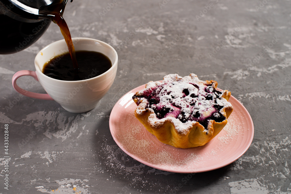 Fresh black coffee is poured into a cup. Cake basket with cottage cheese and berries, sprinkled with powdered sugar. Breakfast on the background of a concrete table.