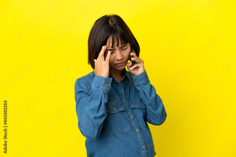 Pregnant woman using mobile phone isolated on yellow background with headache Pregnant woman using mobile phone isolated on yellow background with headache