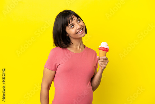 Pregnant woman holding a cornet ice cream isolated on yellow background thinking an idea while looking up © luismolinero
