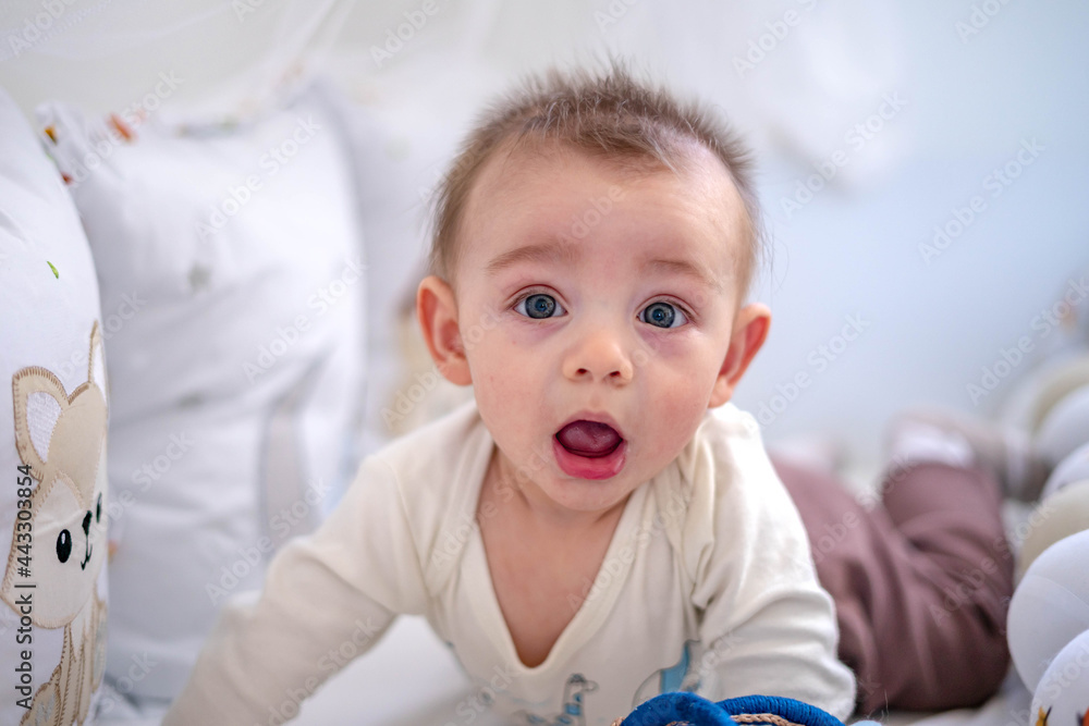 Bebê de olhos claros brincando de morder brinquedo olhando para a câmera no berço claro Bebê de olhos claros brincando de morder brinquedo olhando para a câmera no berço claro