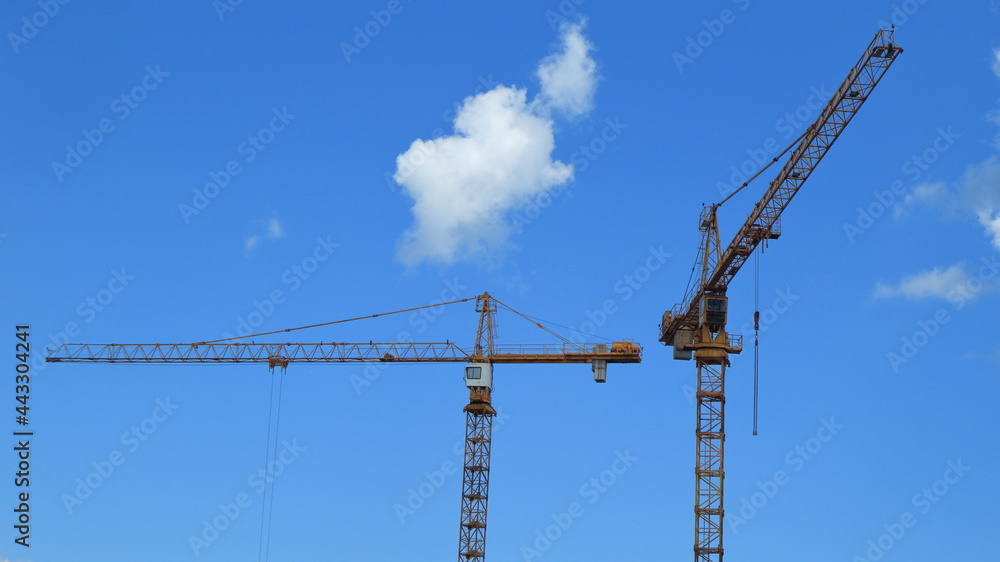Tall construction cranes against a blue cloudy sky do their job with heavy loads. Tall construction cranes against a blue cloudy sky do their job with heavy loads.