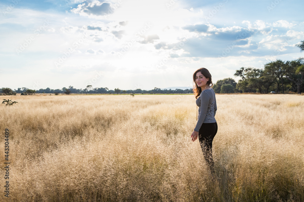 Young adult smiling Mexican woman standing in a dry grassy meadow looking back at the camera