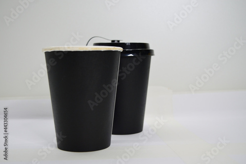 Two black disposable cardboard cups for hot drinks, one closed with a lid