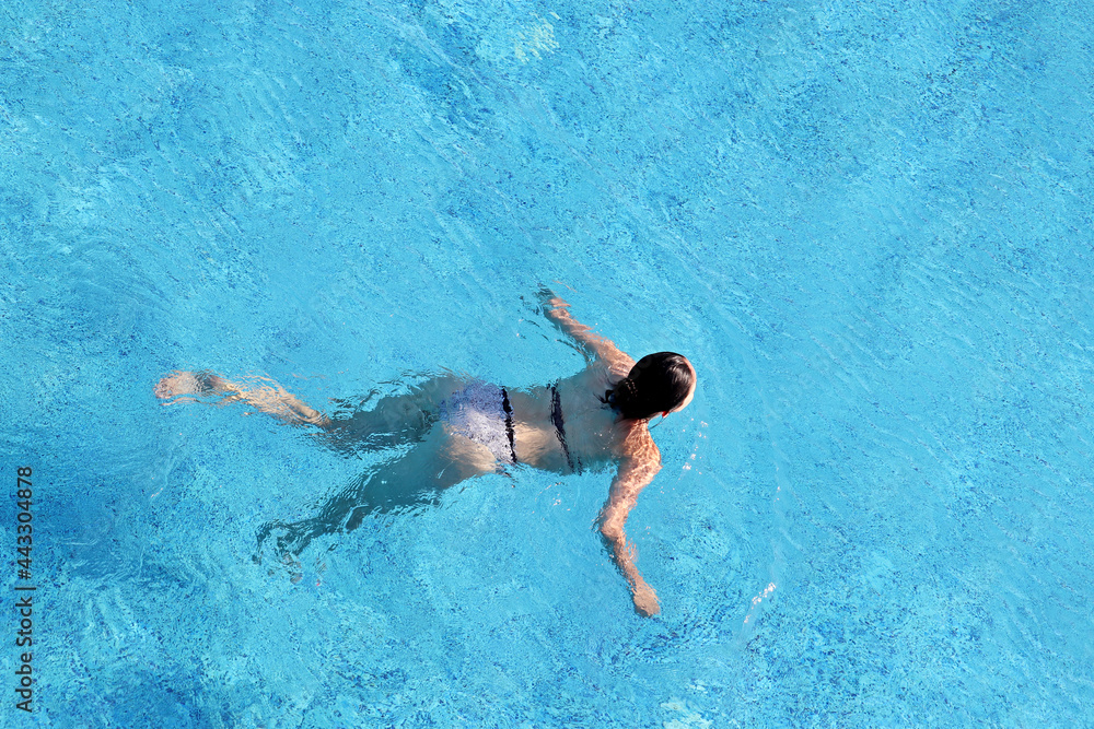 Young woman in a swimsuit swimming in the pool, top view. Water sports, beach vacation