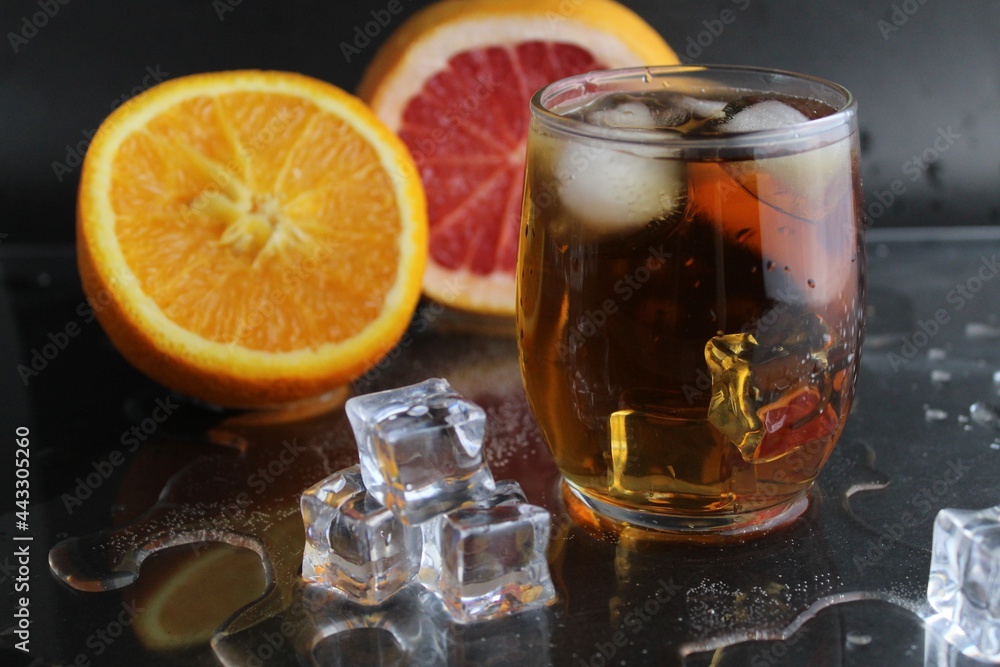 Apple citrus dark juice in a glass next to lies citrus orange grapefruit ice on a black background. Refreshing drinks, summer, soft drinks Apple citrus dark juice in a glass next to lies citrus orange grapefruit ice on a black background. Refreshing drinks, summer, soft drinks
