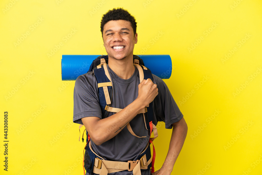 Young mountaineer African American man with a big backpack isolated on yellow background celebrating a victory Young mountaineer African American man with a big backpack isolated on yellow background celebrating a victory