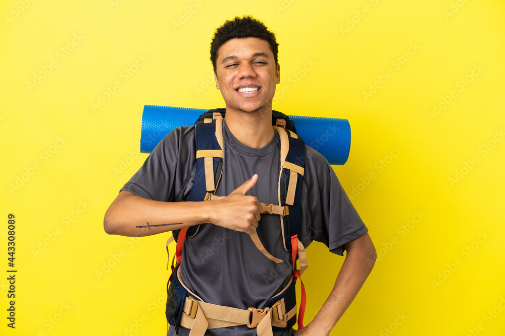 Young mountaineer African American man with a big backpack isolated on yellow background giving a thumbs up gesture Young mountaineer African American man with a big backpack isolated on yellow background giving a thumbs up gesture