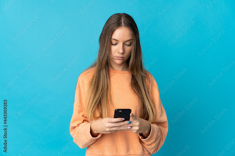 Young Lithuanian woman isolated on blue background using mobile phone Young Lithuanian woman isolated on blue background using mobile phone