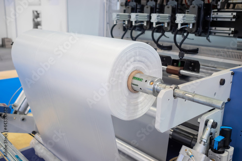 Moving roller with flat polyethylene transparent film - automatic plastic bag making machine at exhibition, trade show. Recycling, manufacturing, industry, automated technology equipment concept