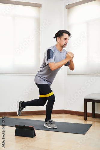 Middle aged man with beard doing exercise at home looking at video on tablet